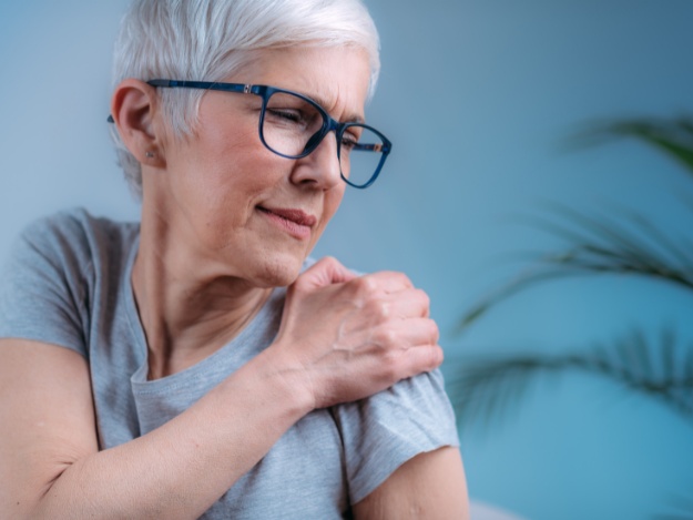 woman with frozen shoulder placing her hand on her shoulder with pain