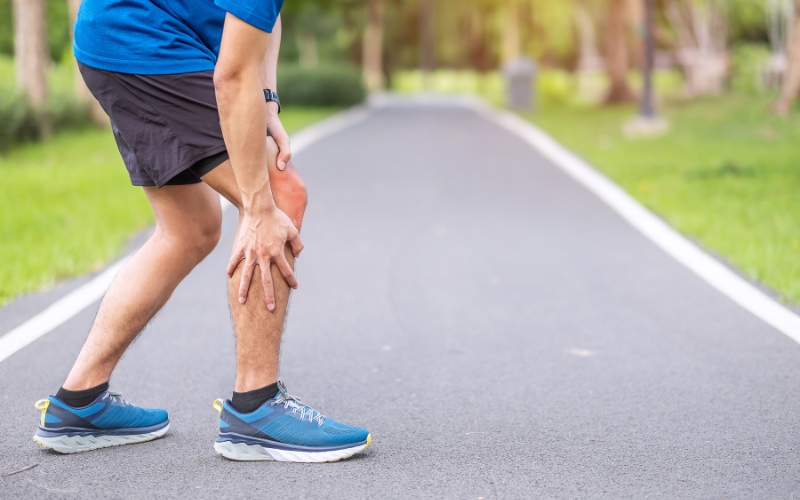 Man in running shoes holding his knee in pain