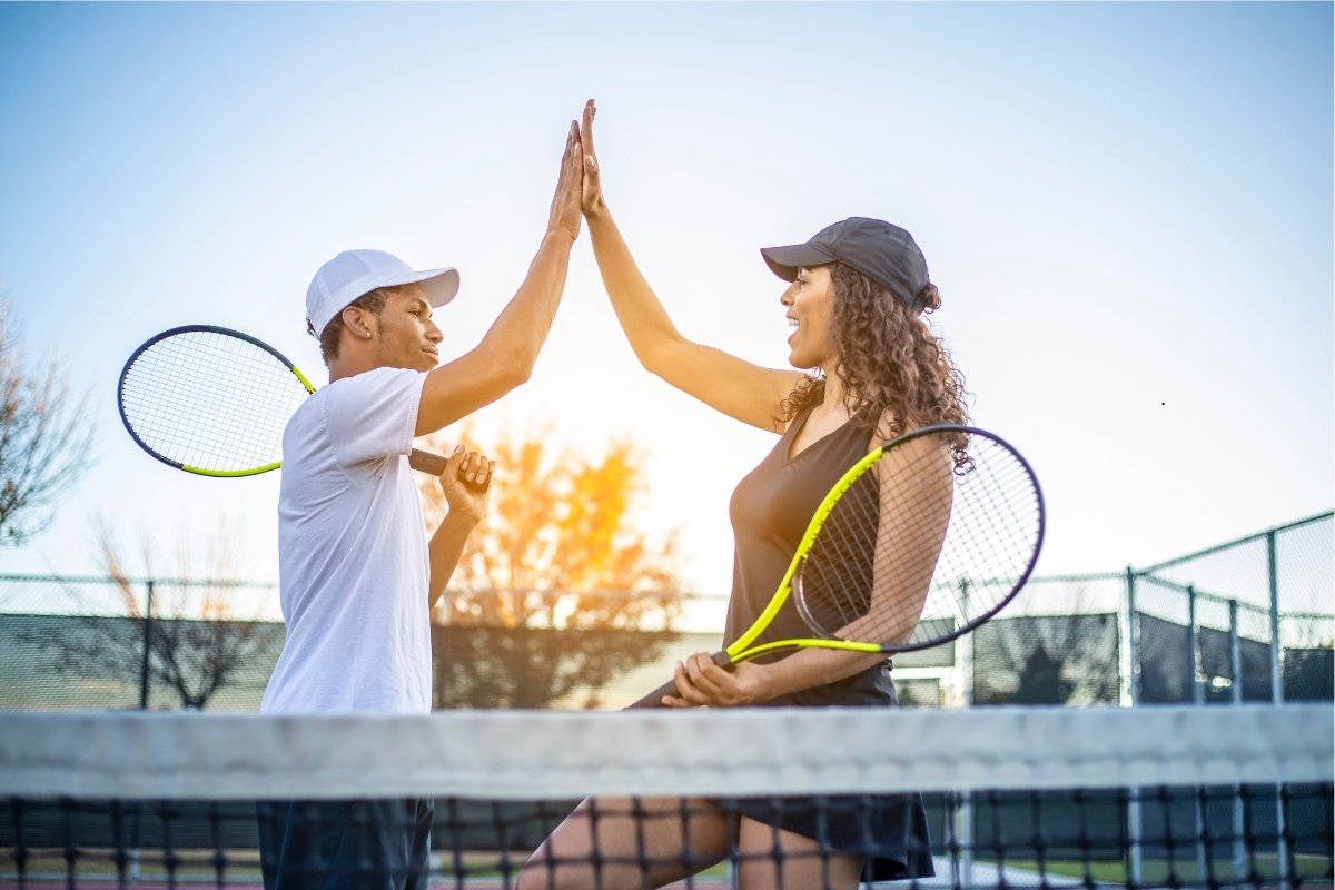 A woman and a man high fiving during a game of tennis