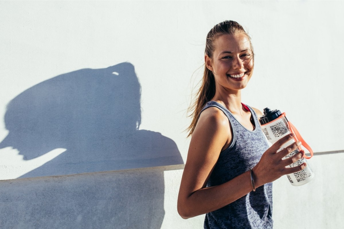 Female athlete smiling with a water bottle, facing the sun