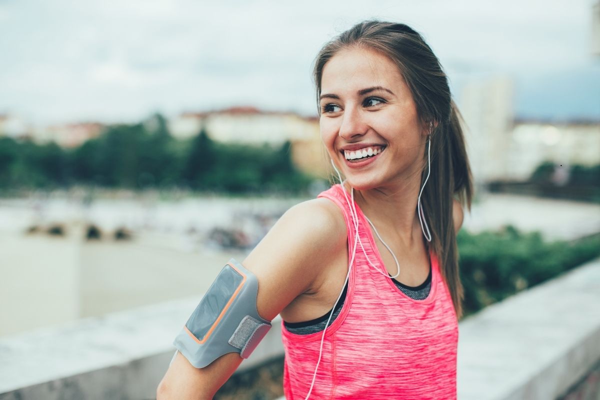 Female athlete smiling with exercise device strapped to arm, in front of a river bridge