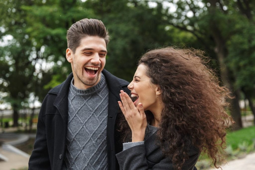 Male and female sharing a laugh walking through a park (1)