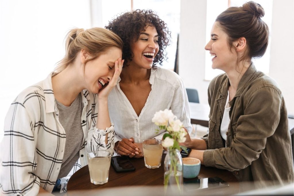 Three females having a laugh at a table with coffee