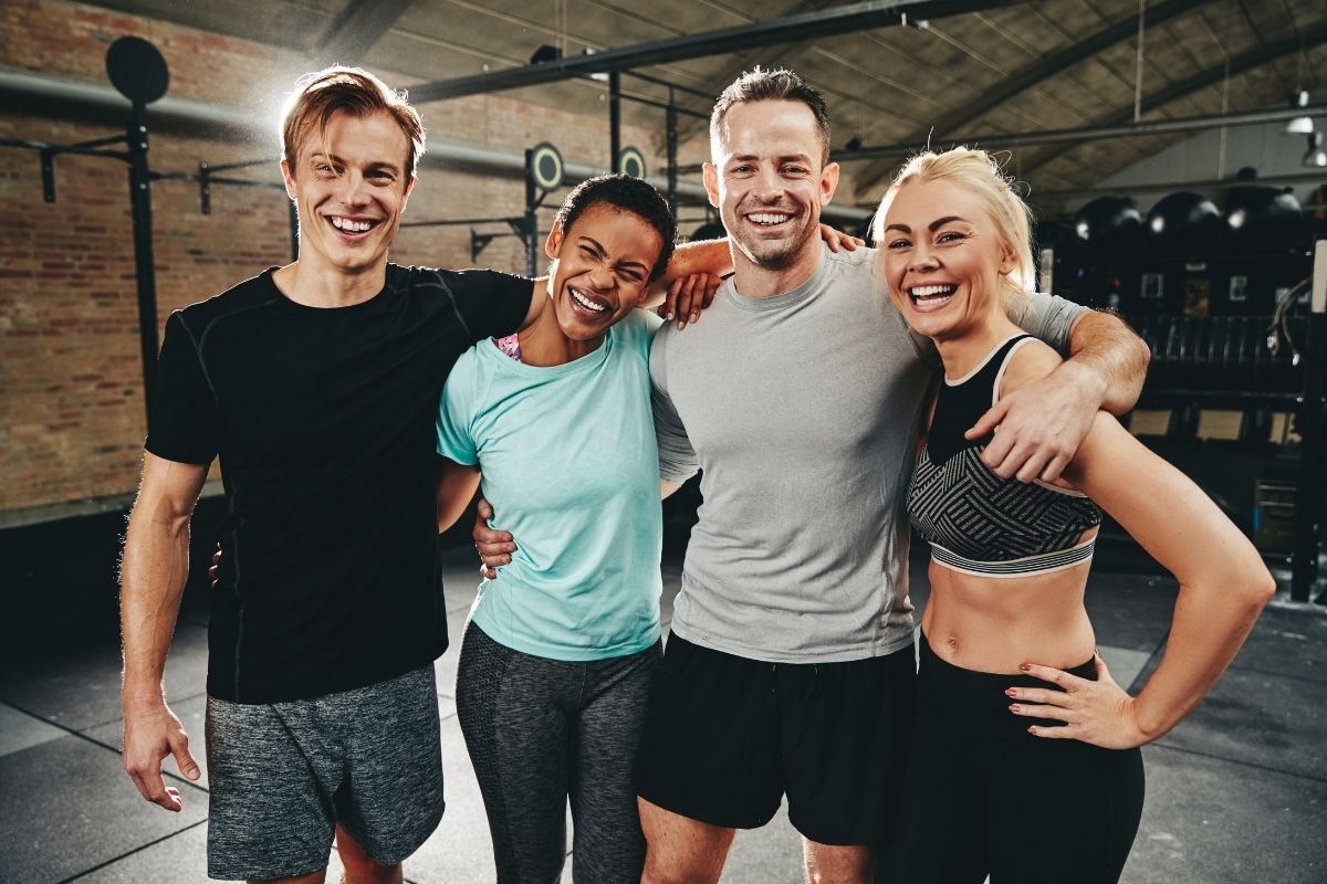 Two men, and two women posing for a group photo during a workout at the gym