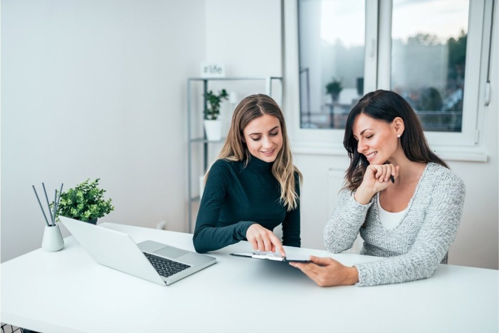 Two women sat at a table with a laptop and a report