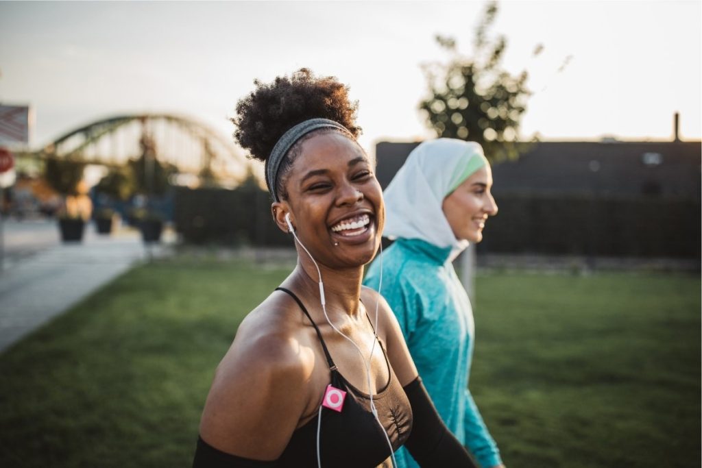 Women smiling at the camera walking on grass with earphones in