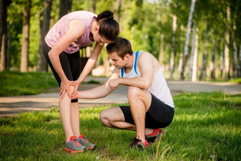 Female holding her injured knee and being assisted by male