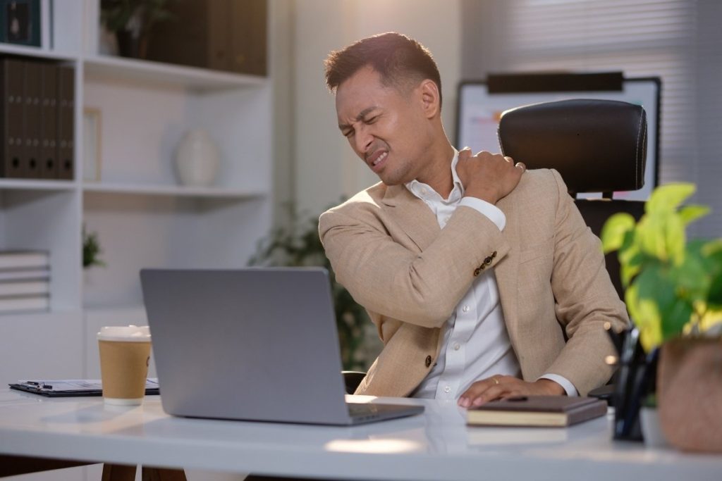 Man holds hurt shoulder at desk