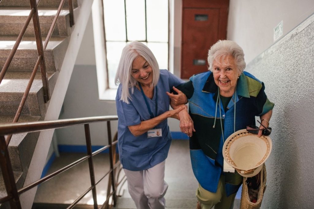 Elderly female patient helped up the stairs by female health worker