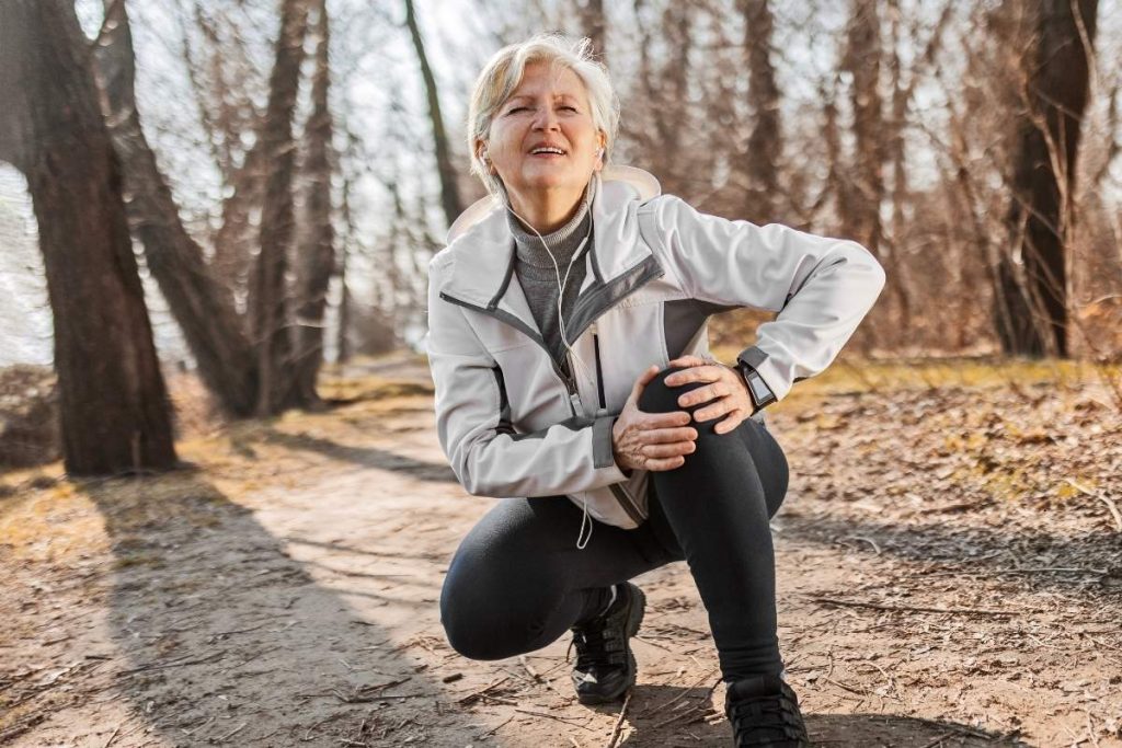 Woman kneeling down holding left knee whilst on walk